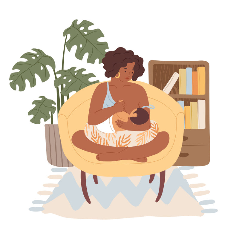 A mother sitting cross-legged on a chair, breastfeeding her baby