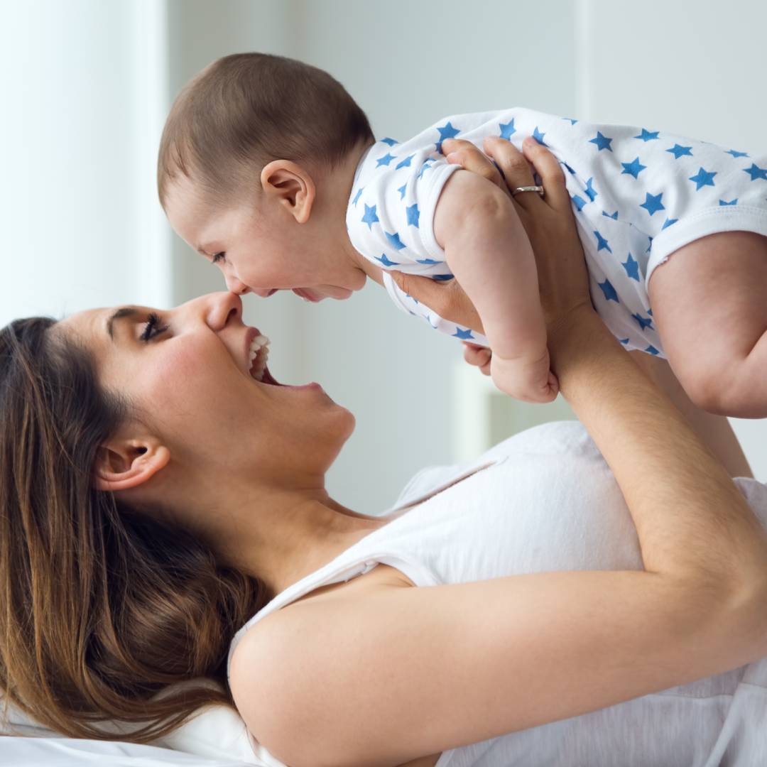 A laughing mother holds her smiling baby above her face 